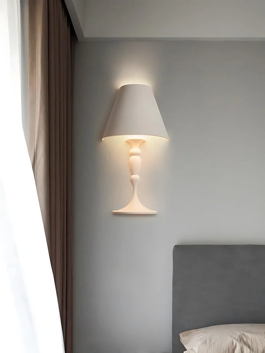 Sculptural wall sconce mounted beside a bed and upholstered headboard