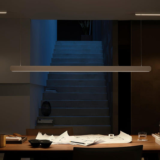 Warm linear pendant above papers on a dark worktable