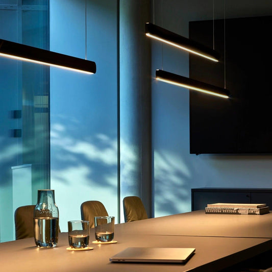 Black linear pendants above a worktable beside tall windows
