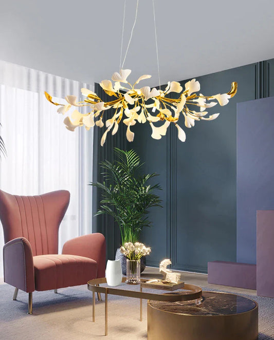 White and gold ginkgo chandelier above a lounge with a pink chair and indoor plant