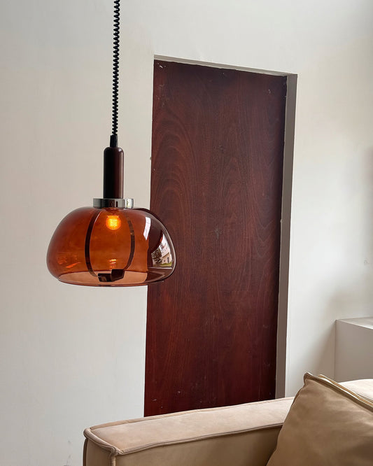 Amber glass pendant glowing beside a sofa and dark wood wall