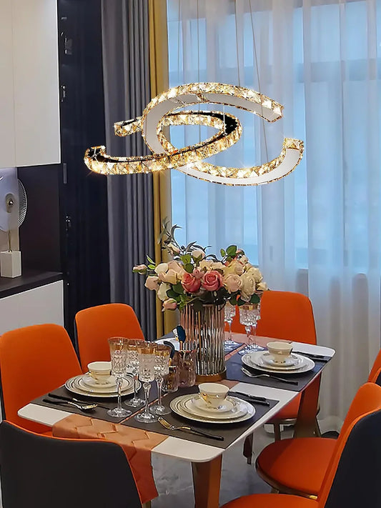 Modern Double C Crystal Chandelier above a dining table with orange upholstered chairs